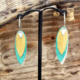 Pair of earrings with gold and turquoise design on a wooden background